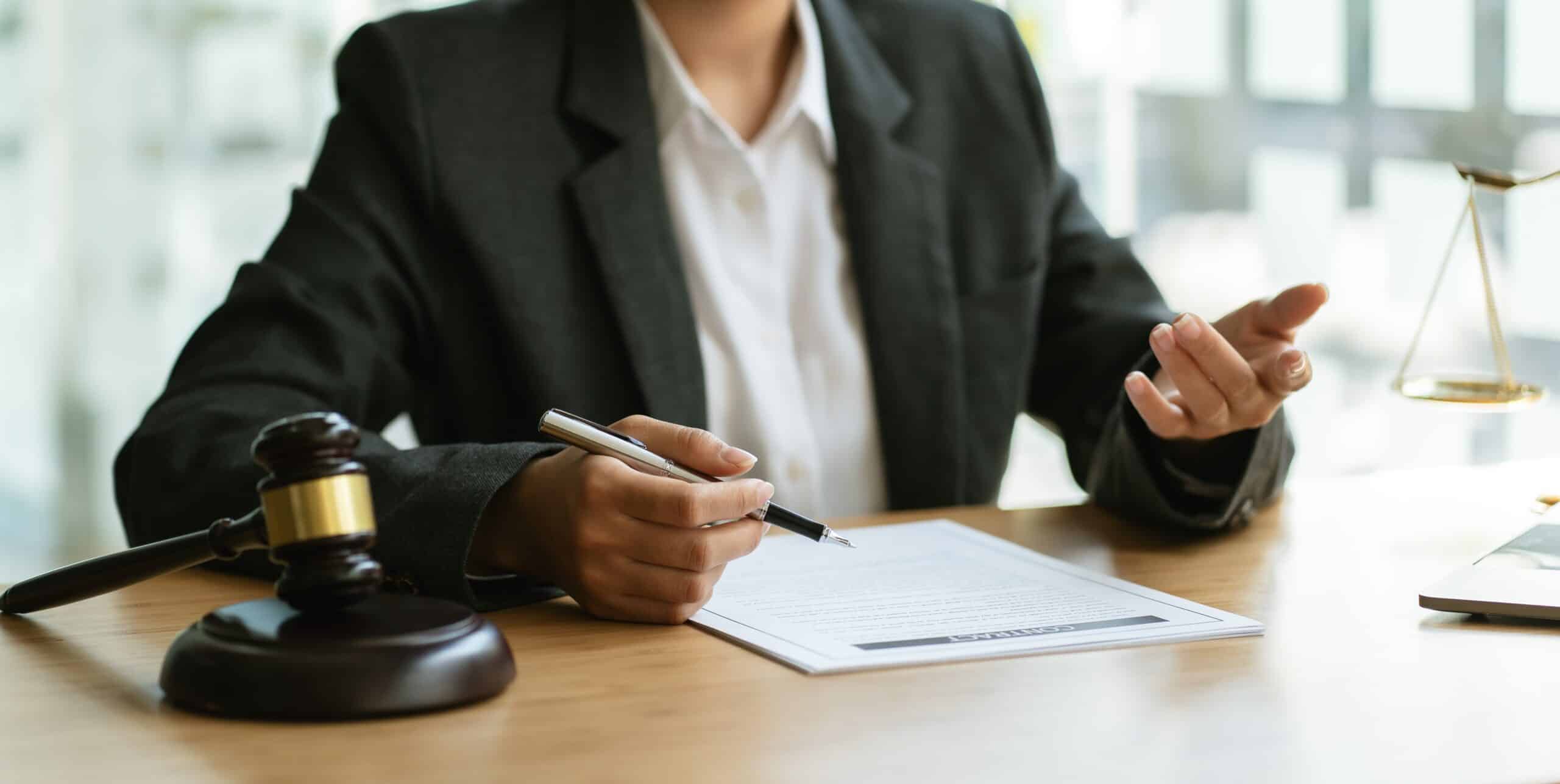 Woman sitting at a desk, holding a pen to sign a contract for a real estate attorney in Nassau County.