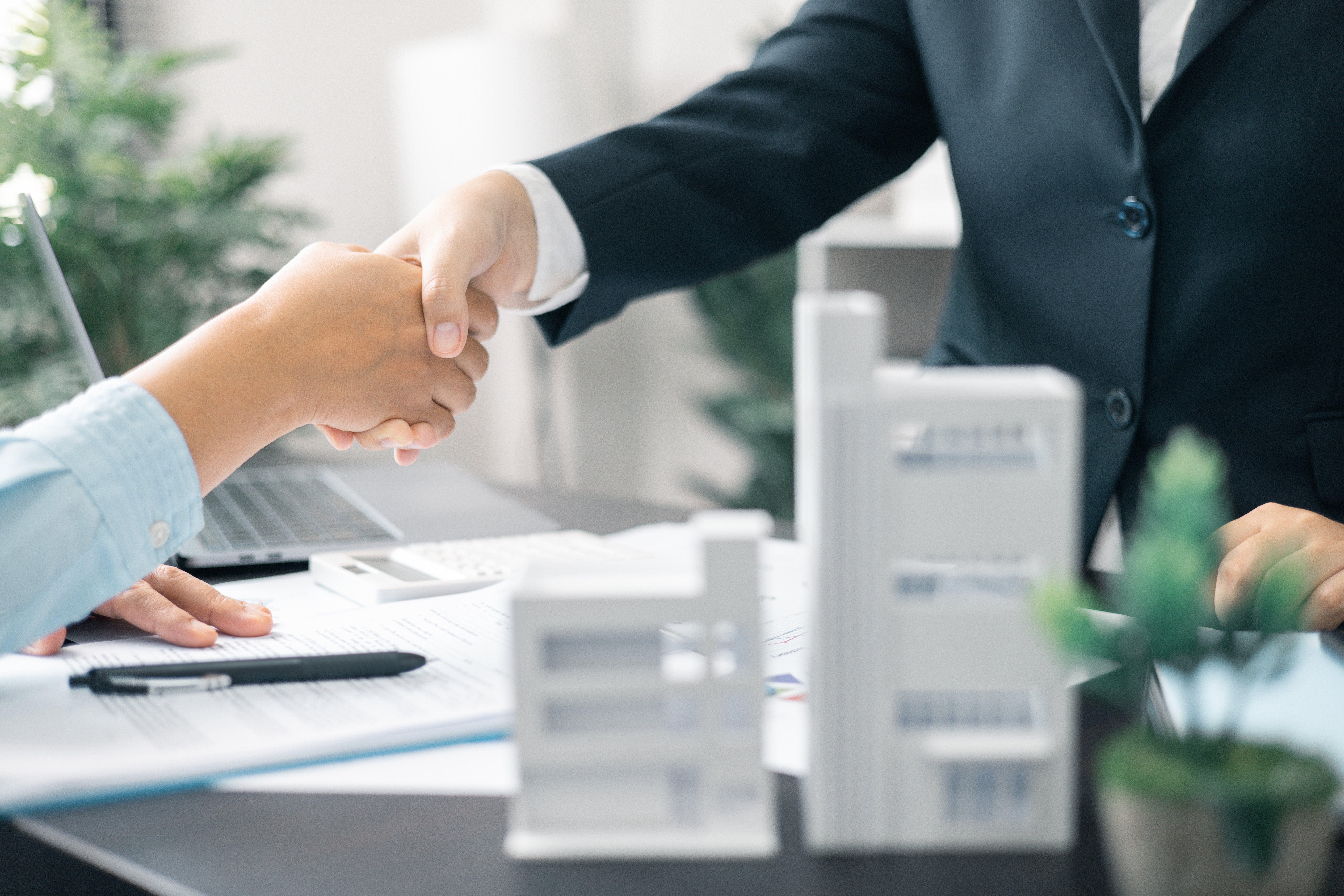 Two people shaking hands over a desk with a real estate contract resting in front of the Nassau County real estate attorney.