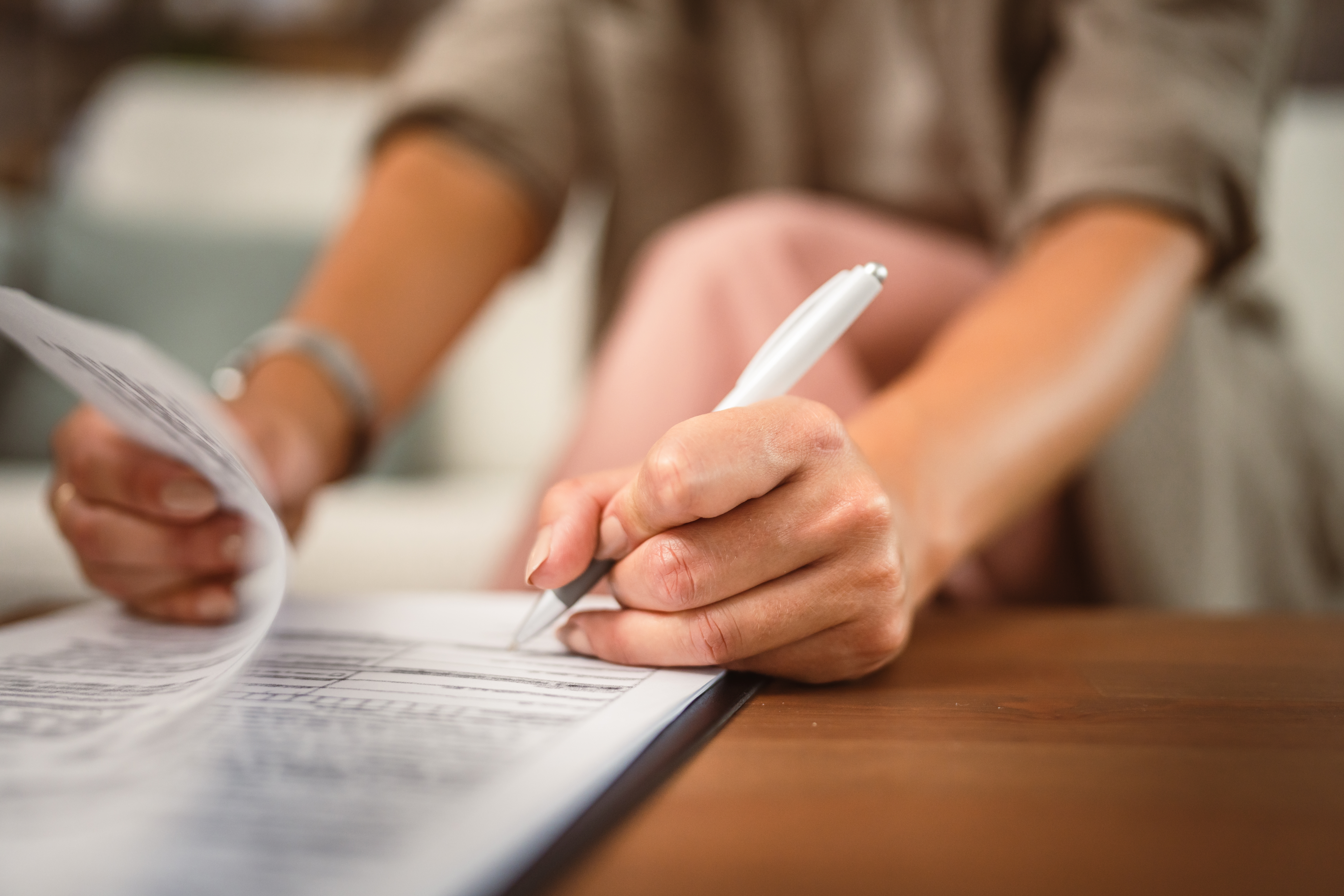 Close up of a woman holding a pen and signing the closing documents for her home purchase in Nassau County.